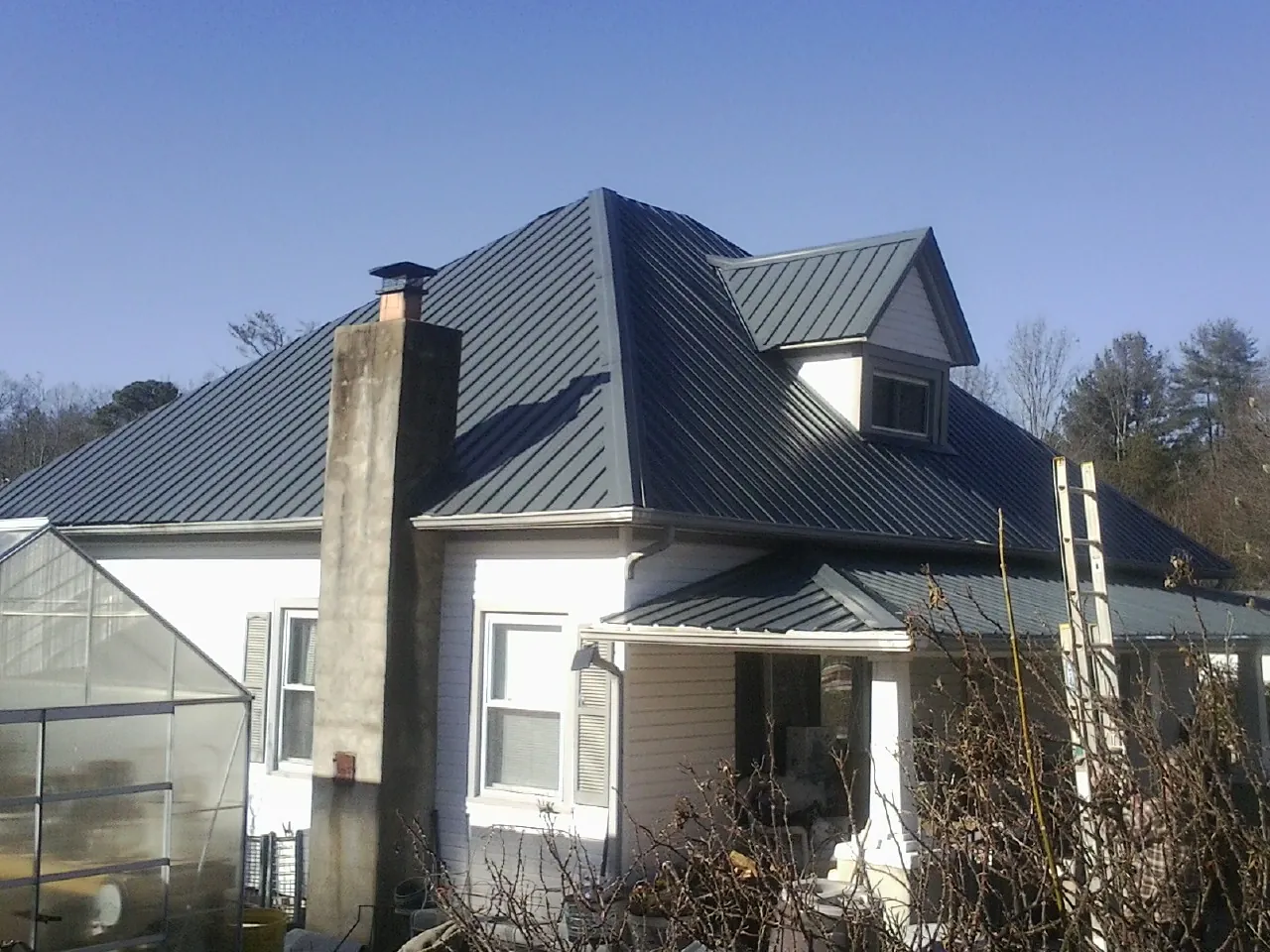 Dark blue standing seam metal roof on a white farmhouse with dormer — Slate & Tile Roof Repair by Roofing Brothers in Footville