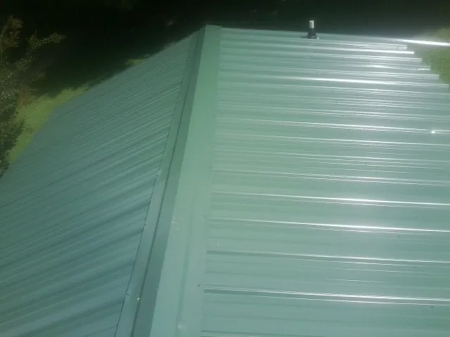 New green metal panels meeting at the ridge of a roof — Flat Roof Repair work by our crew in Footville