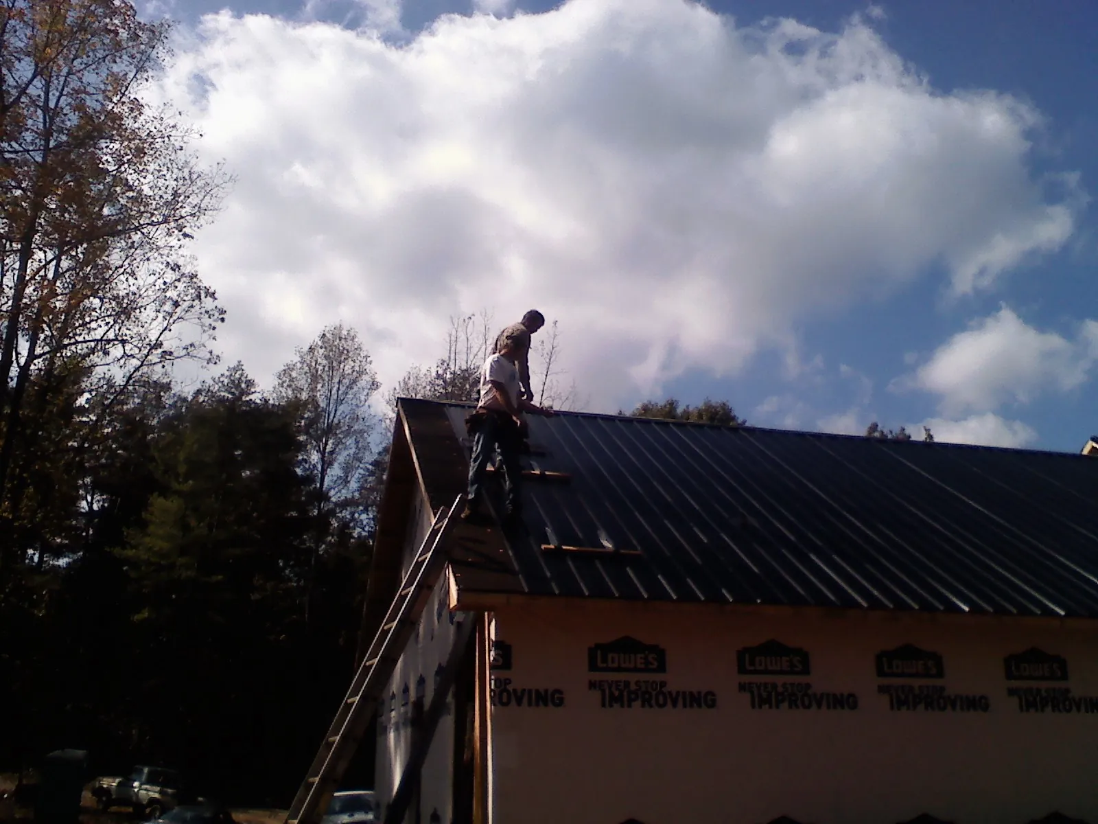 Roofer fastening dark metal panels high against a cloudy sky, from a Roof Inspection job in Footville