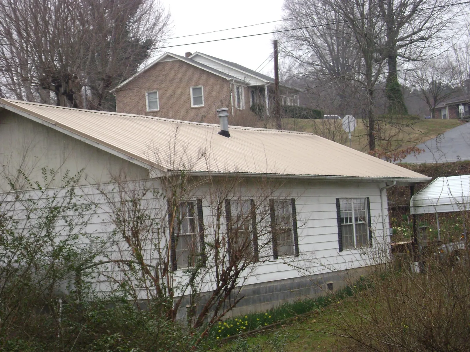 Tan metal roof on a white sided house set into a hillside — Commercial Roofing by Roofing Brothers in Footville